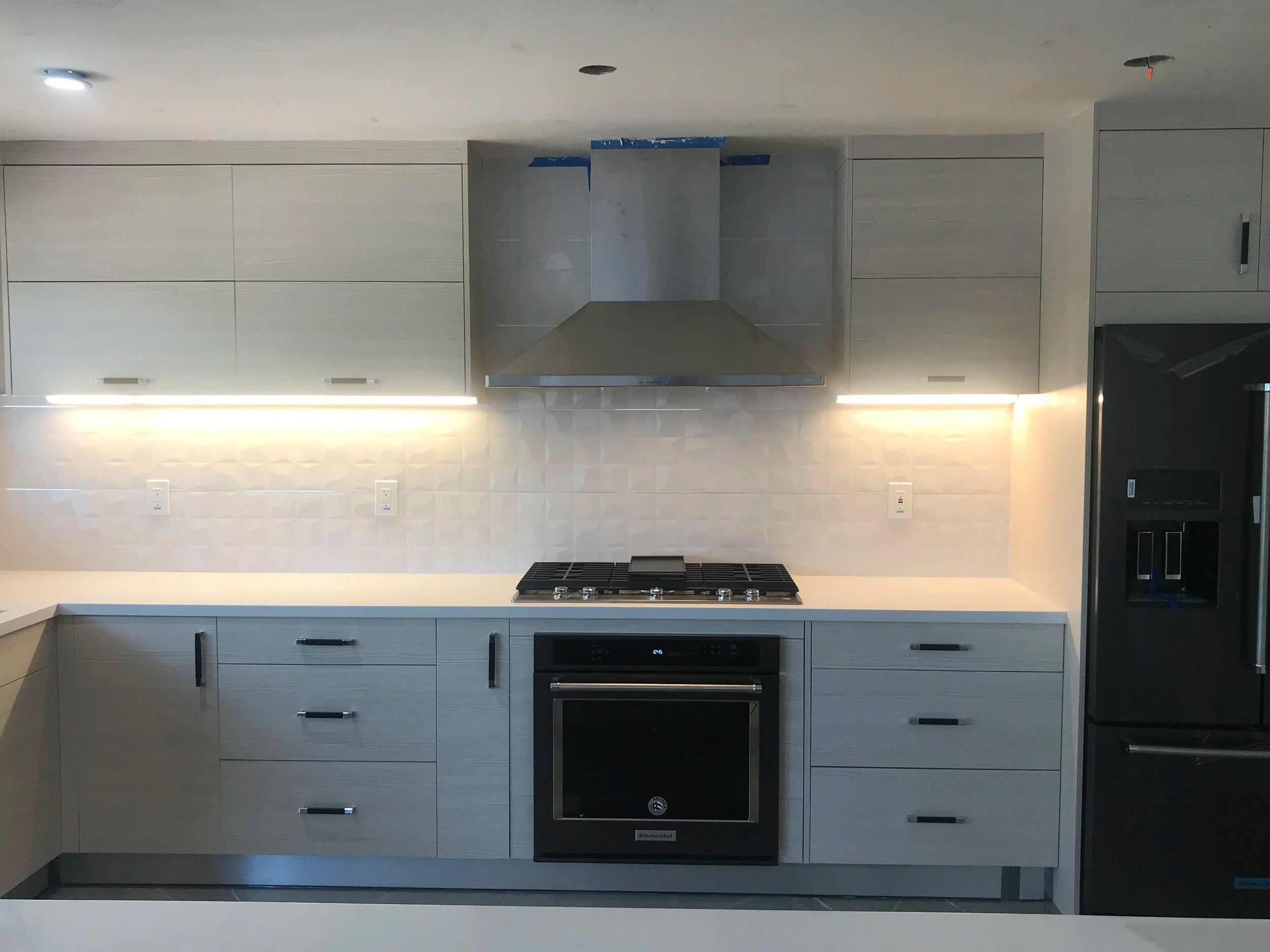 Remodeled kitchen with two-tone flat panel cabinets, a stainless range hood, gas cooktop and under-cabinet lighting.