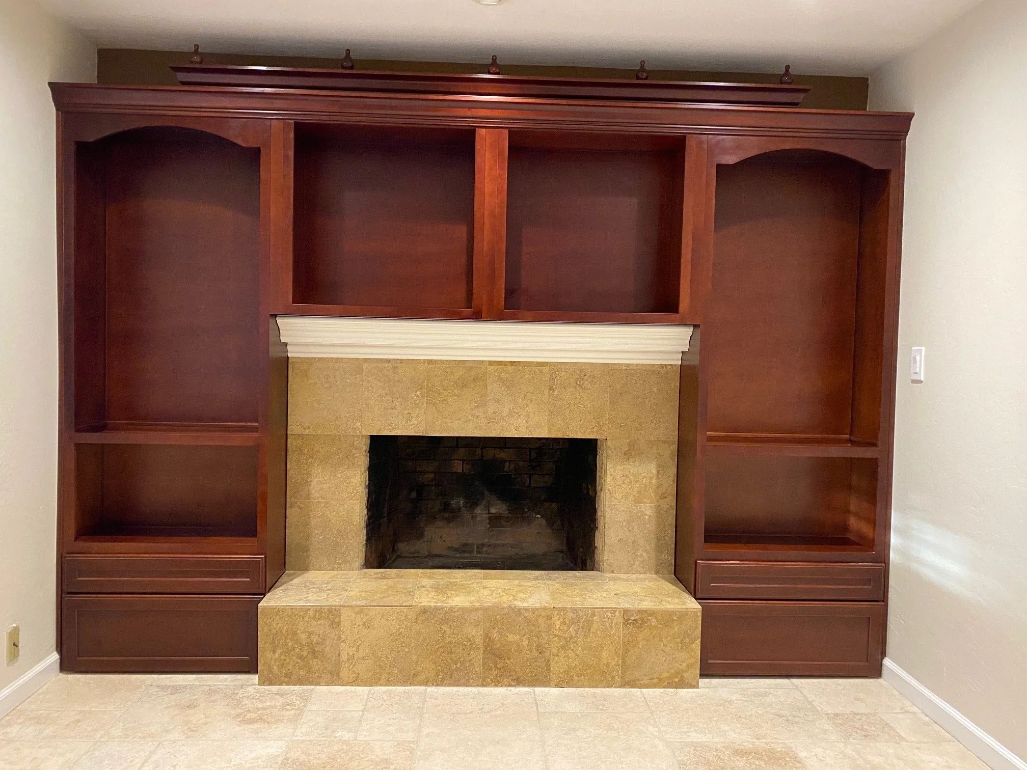 Built-in cherry cabinetry and shelving surrounding a travertine fireplace, with lighting fitted into the upper shelves.