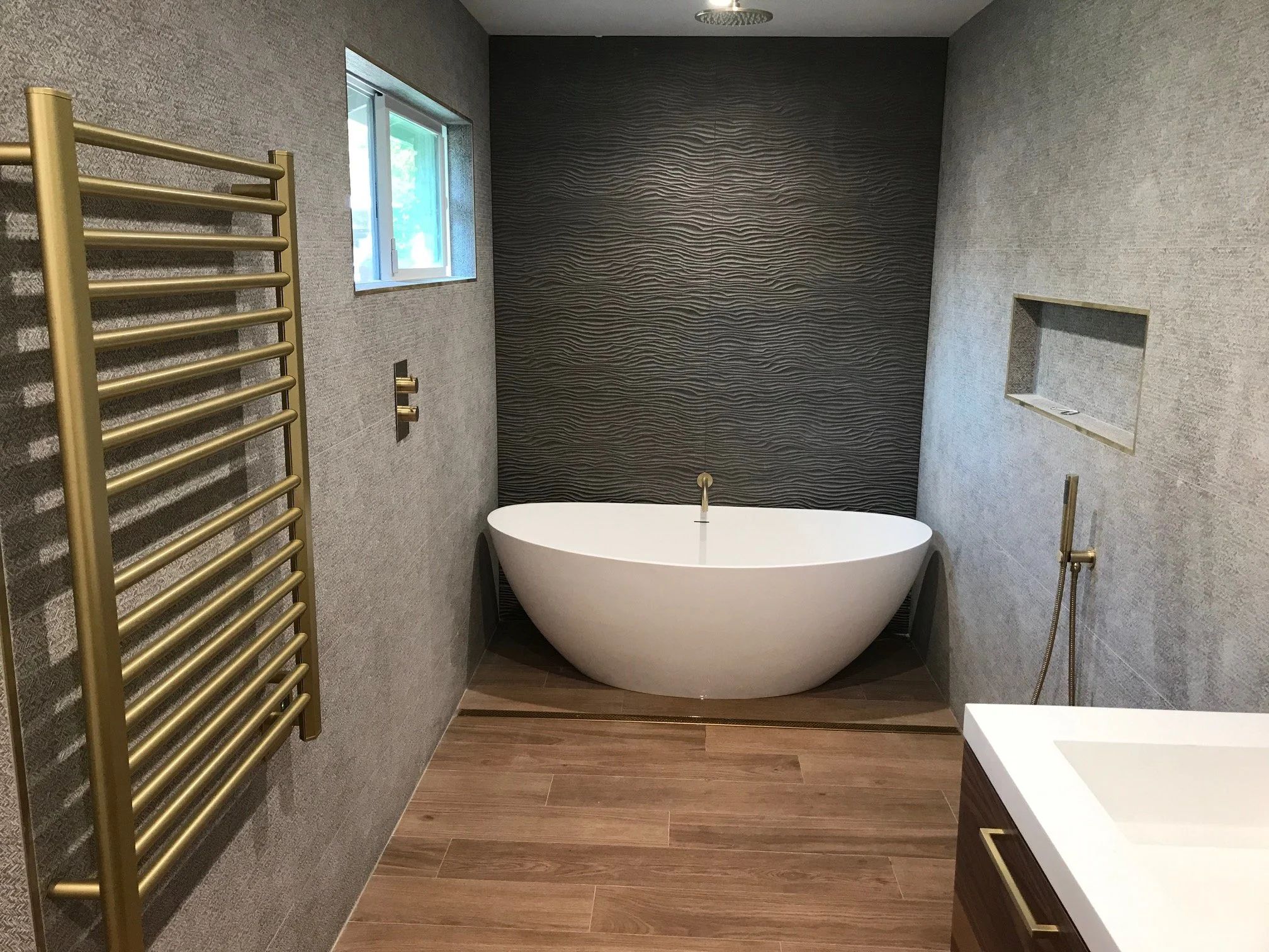 Remodeled bathroom with a freestanding soaking tub, a textured charcoal accent wall, brass fixtures and a heated towel rail.