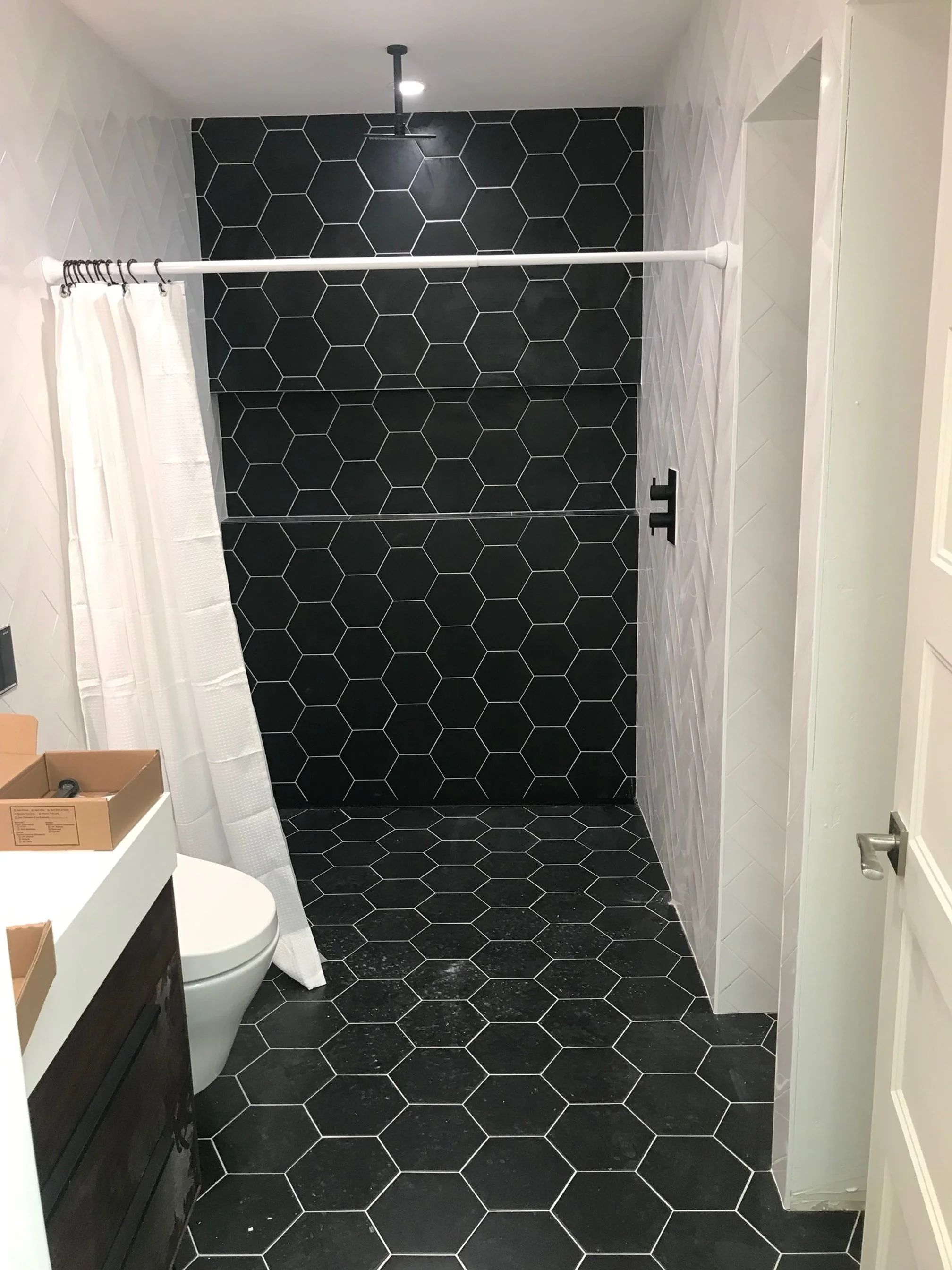 Remodeled bathroom with black hexagon floor and shower tile, white wall tile, and matte black shower fittings.