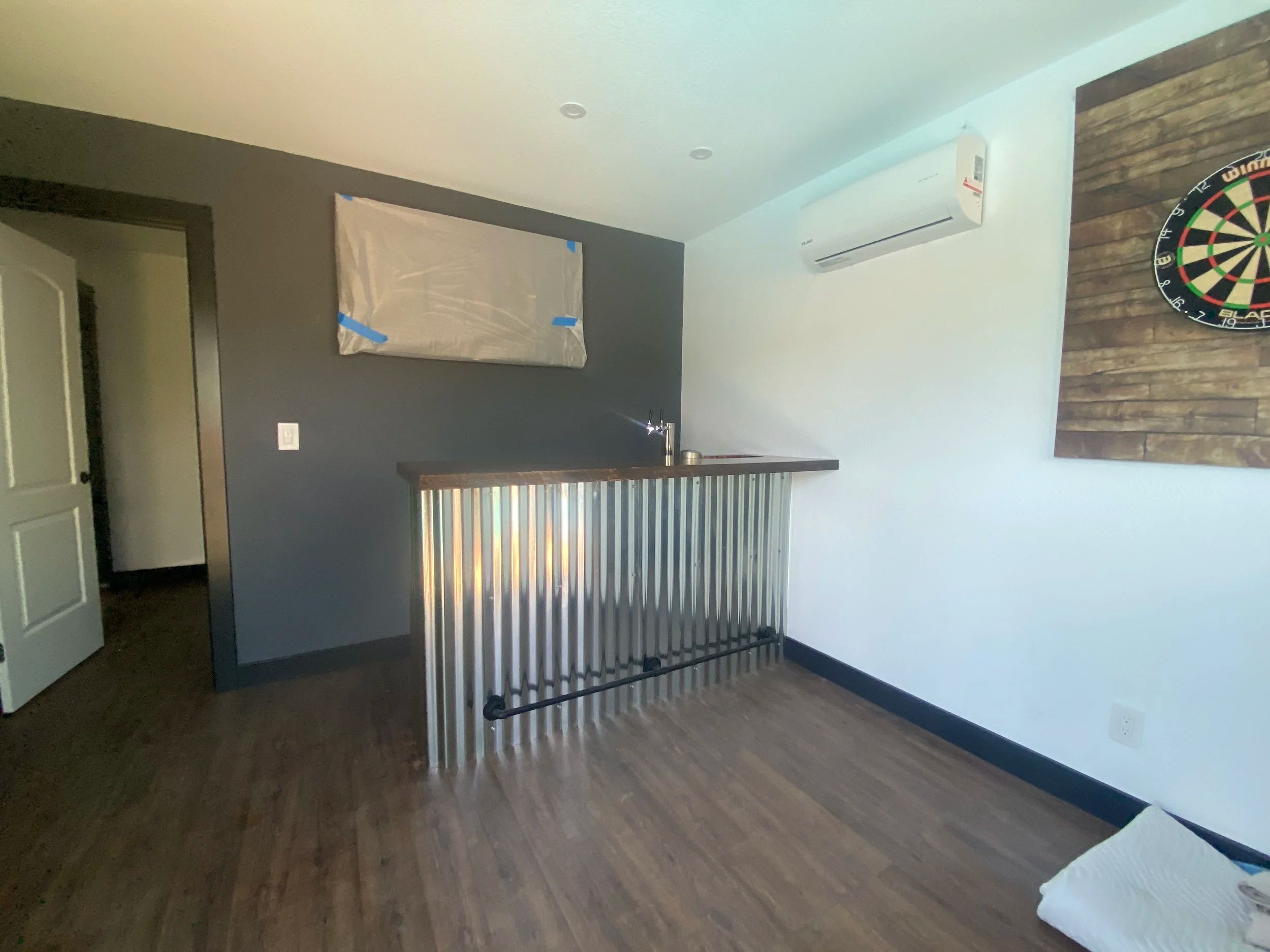 Converted room with a corrugated metal bar front, a timber bar top, a wall-mounted heat pump and plank flooring.